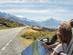 A woman pulled over by the side of a road to look at a paper map with snow-capped mountains in the distance
