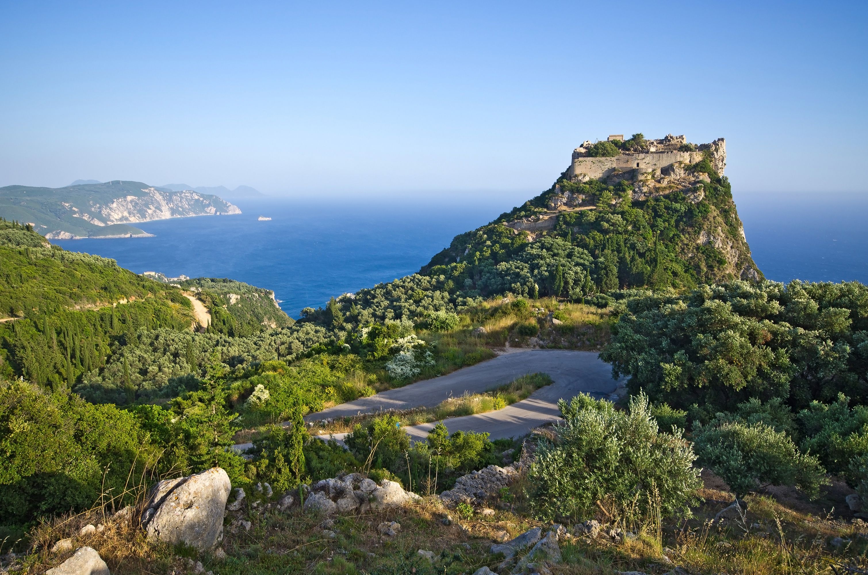 View of the lush, tree-covered landscape towards the old ruins of a fortress high on a hill overlooking the sea