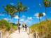 A picture showing a family walking to the beach along a footpath with palm trees, and ocean in the background on a sunny day in South Beach, Miami, Florida, USA