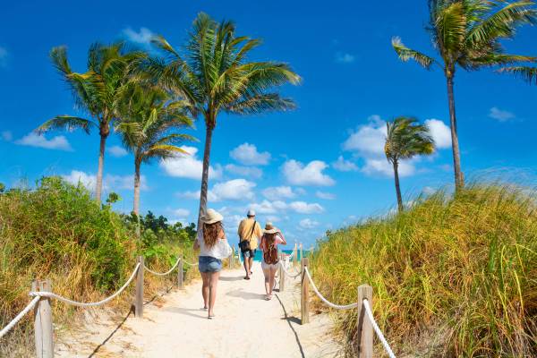A picture showing a family walking to the beach along a footpath with palm trees, and ocean in the background on a sunny day in South Beach, Miami, Florida, USA