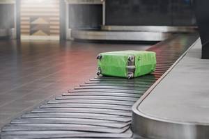 A lone suitcase wrapped in green plastic on the luggage conveyor belt at an airport