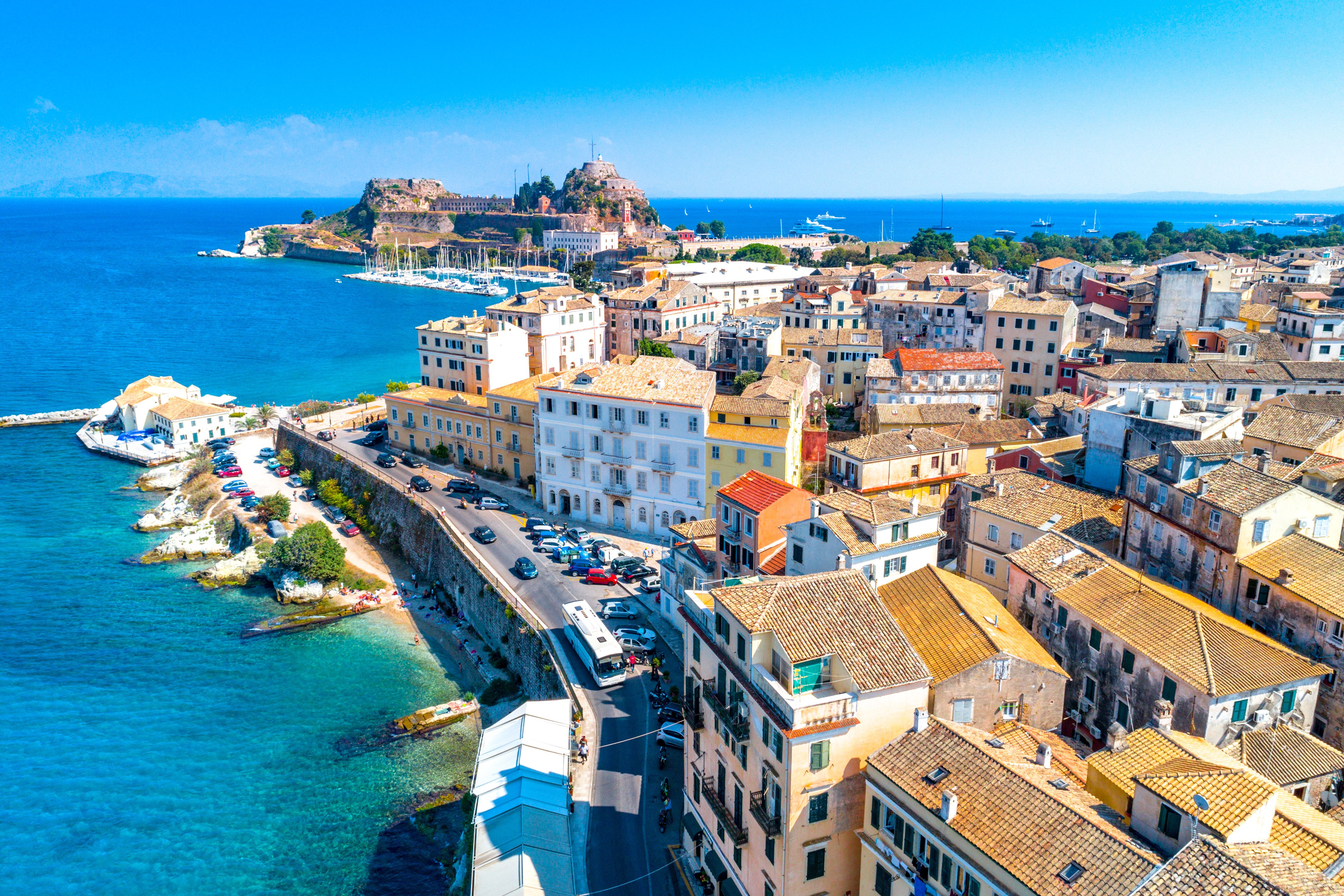 Panoramic view of Kerkyra with pastel yellow buildings in foreground and the Old Fortress of Corfu in the background 
