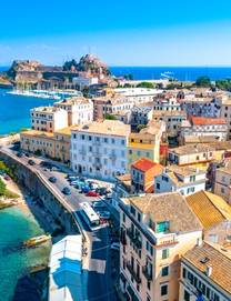 Panoramic view of Kerkyra with pastel yellow buildings in foreground and the Old Fortress of Corfu in the background 