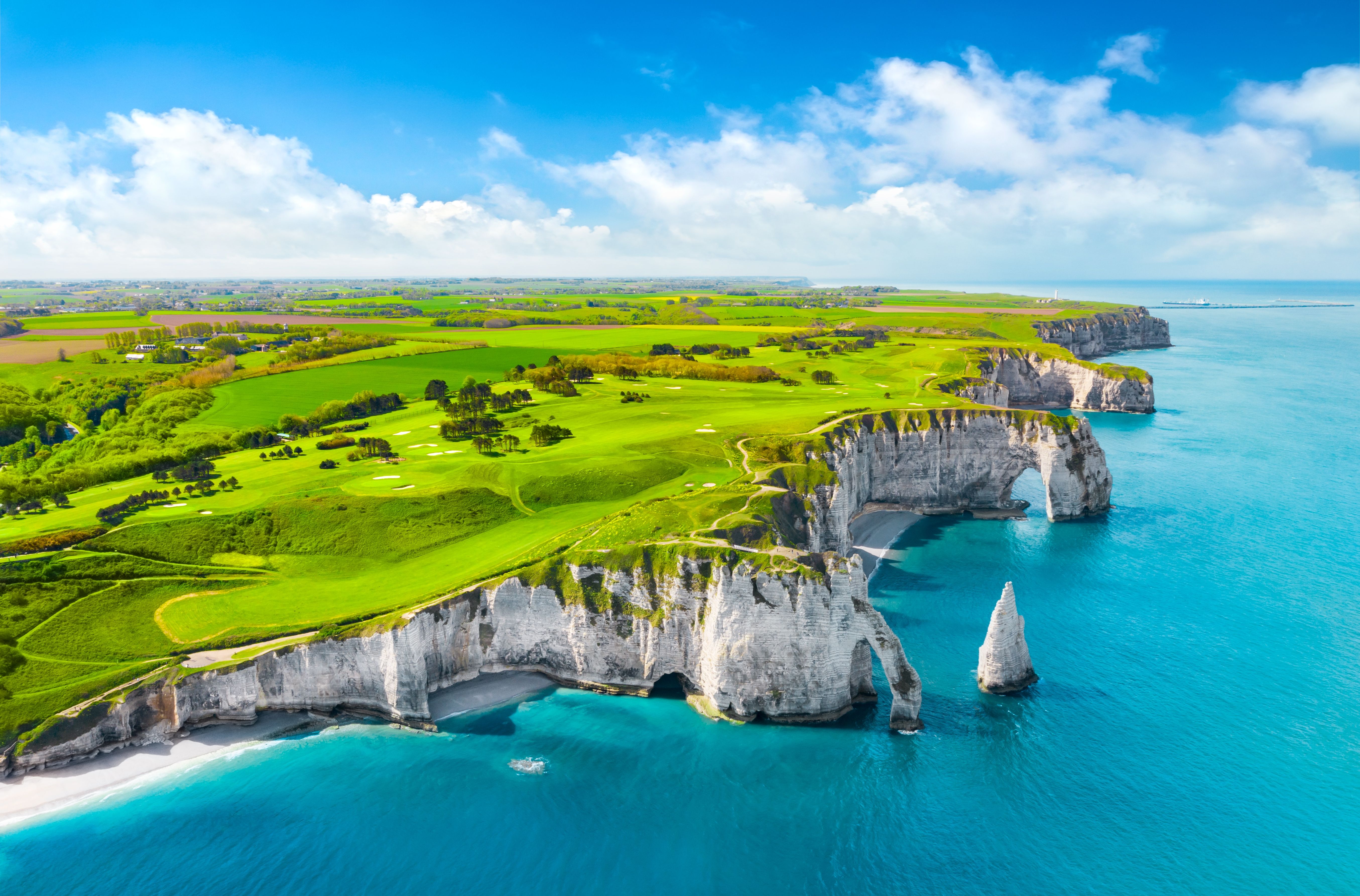 Aerial view of dramatic chalk white cliffs and bright turquoise waters lapping a white-sand beach.