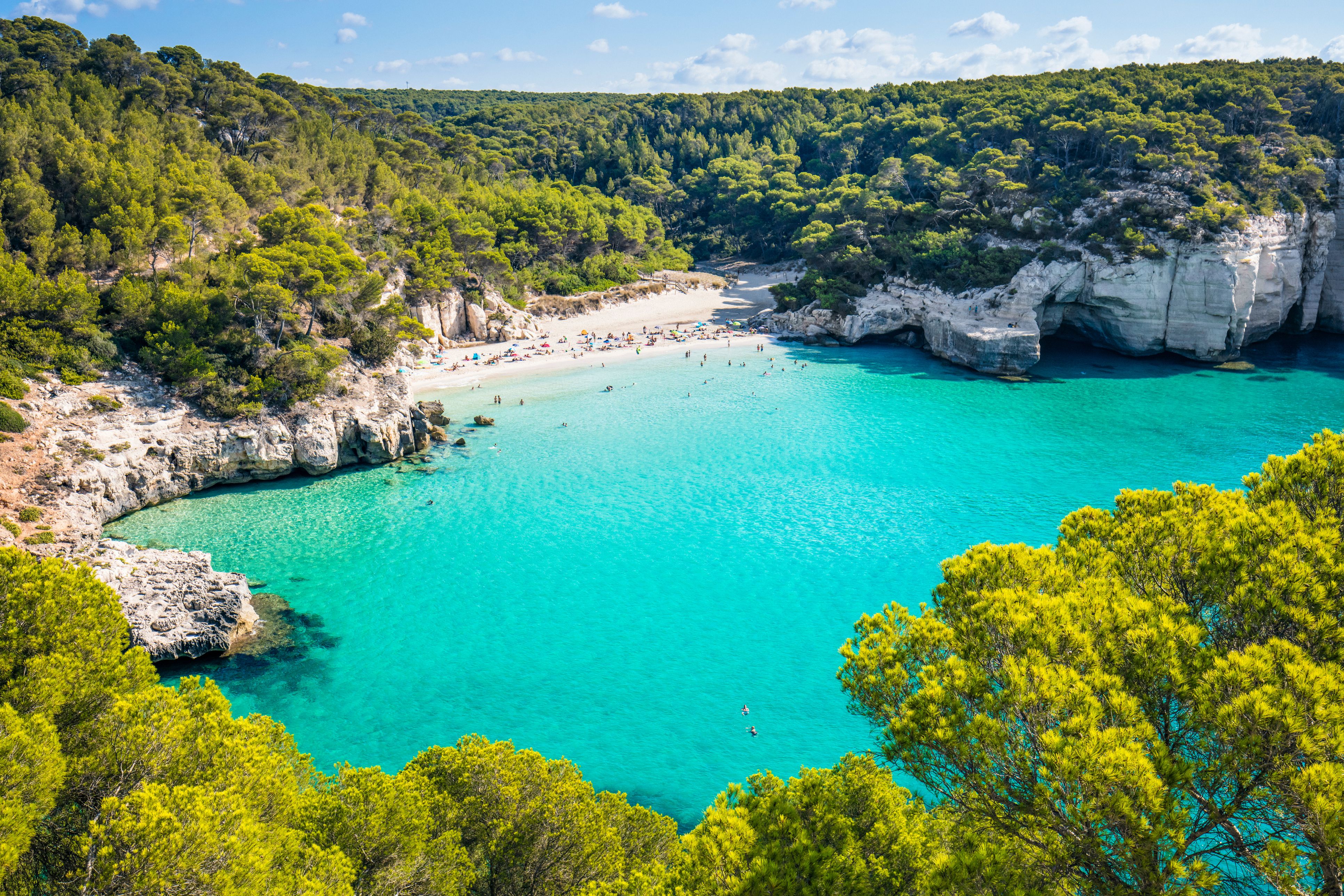 Aerial view of Cala Mitjana beach in Menorca with clear blue water and people swimming, located in the Balearic Islands of Spain