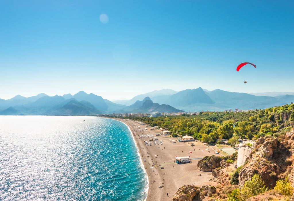 An aerial panoramic view of Antalya and Mediterranean seacoast and beach with a paraglider in Turkey on a sunny summer day with a busy beach