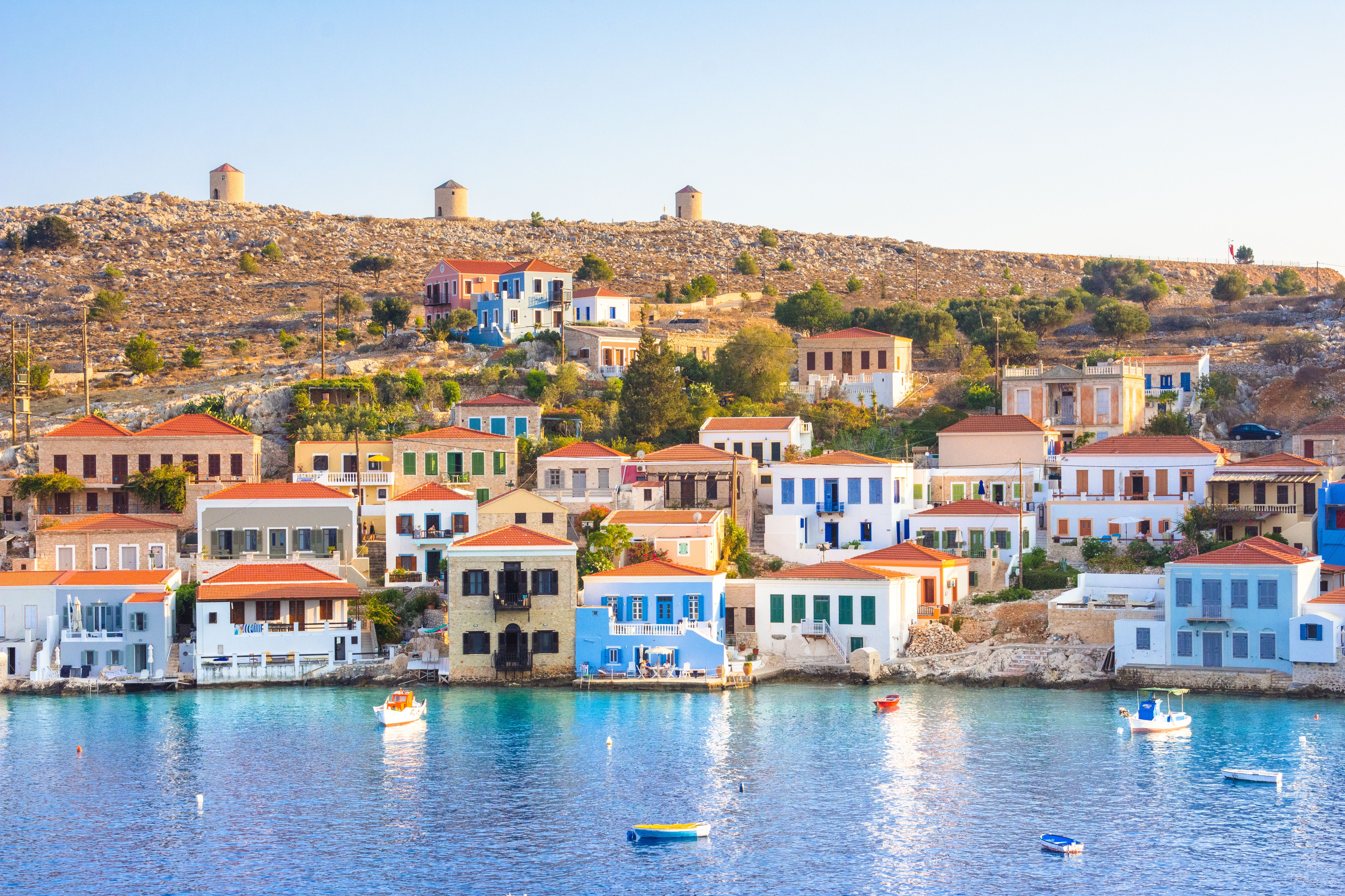 Soft sunlight casts a gentle glow on whitewashed and pastel houses on the water's edge of Chalki island, Greece