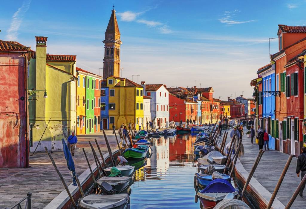 A view of a canal in Venice, Italy lined with colourful boats moored to the side and bordered either side with rainbow-coloured houses