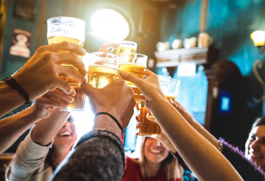 Group of friends drinking and toasting beer with pint glasses in focus