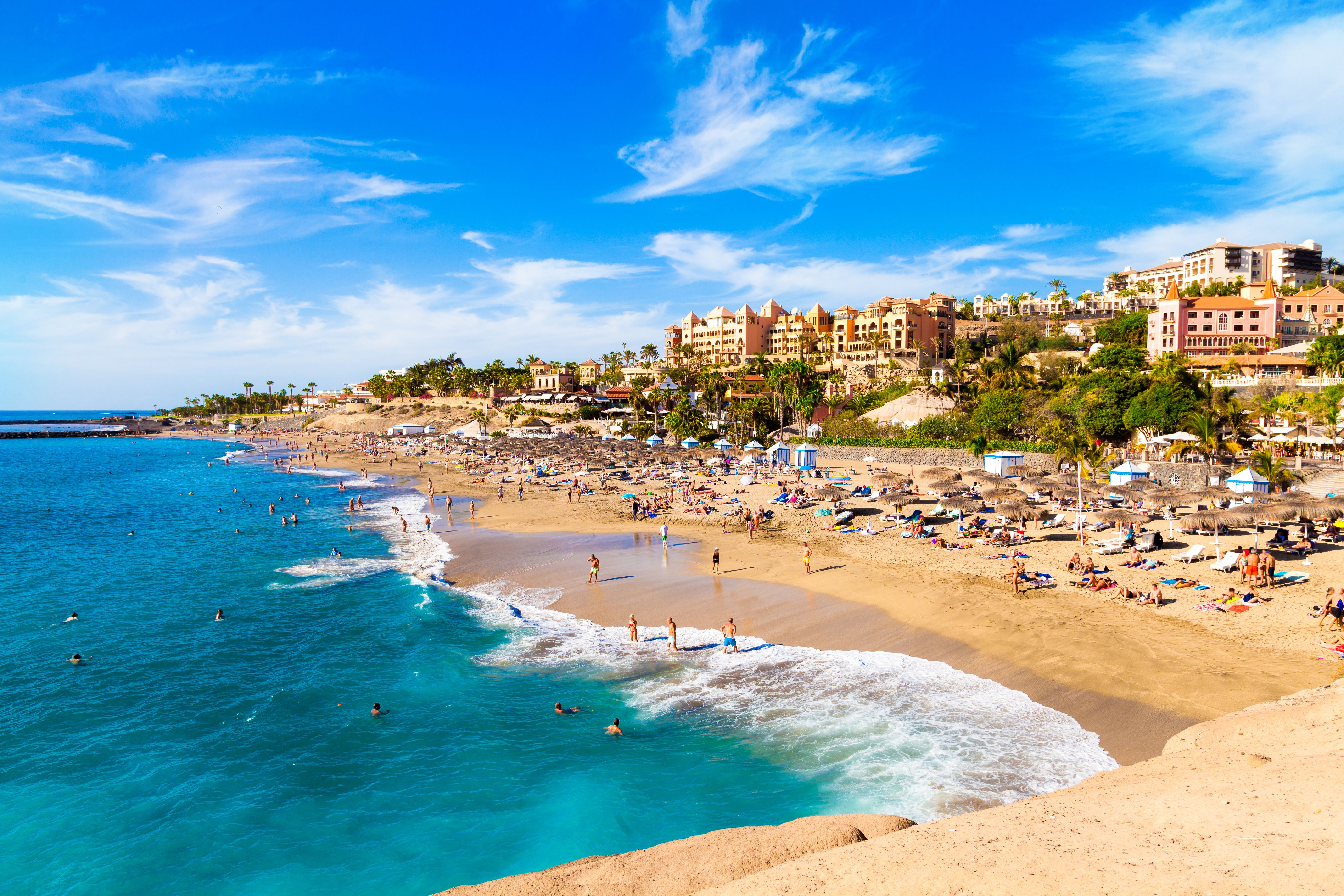 El Duque beach in Tenerife on a sunny day with lots of people on the sand and in the sea