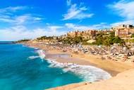 El Duque beach in Tenerife on a sunny day with lots of people on the sand and in the sea