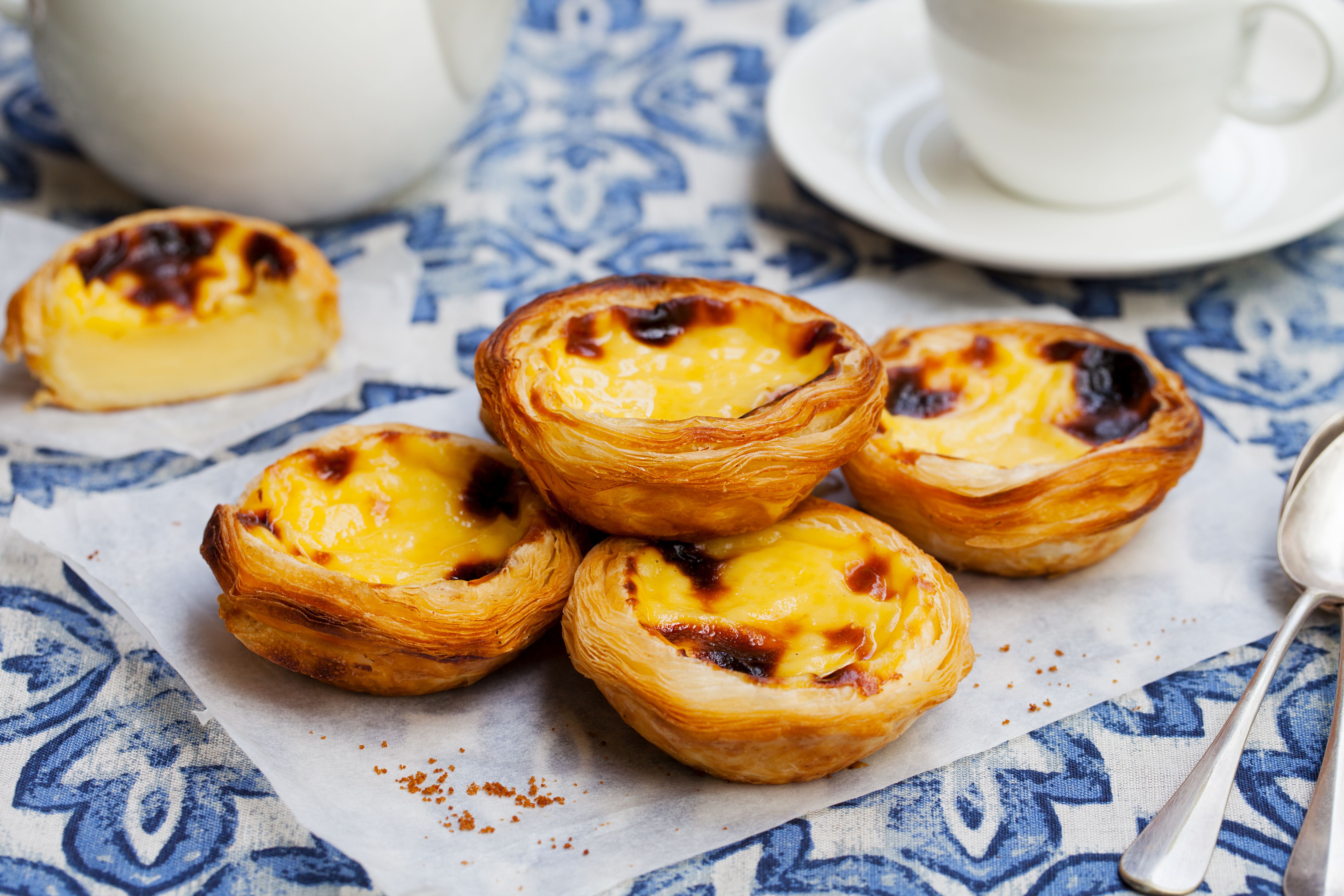 Four flaky pastel de nata on a parchment on a tiled blue table in Lisbon
