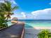 A view of a wooden water jetty extending out into turquoise sea from a white sand beach with palm trees in the Maldives