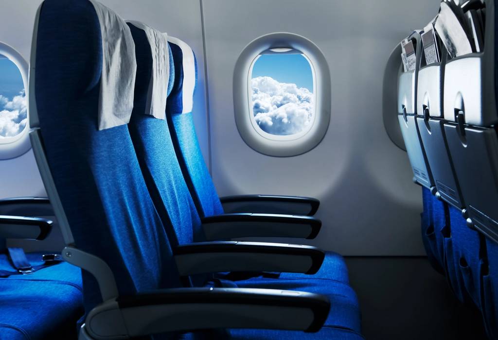 Empty plane seats with window looking out onto blue sky and clouds