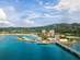 Aerial view of a coastal town in Jamaica with a cruise port, over-water bridge and a long sandy beach, all on a backdrop of tree-filled hills