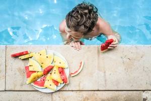 Kid in the swimming pool with a plate of watermelon on the side