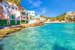 A view of traditional white-washed boathouses, apartments and beach at Playa Santanyi in Majorca with azure-coloured sea and clear blue sky