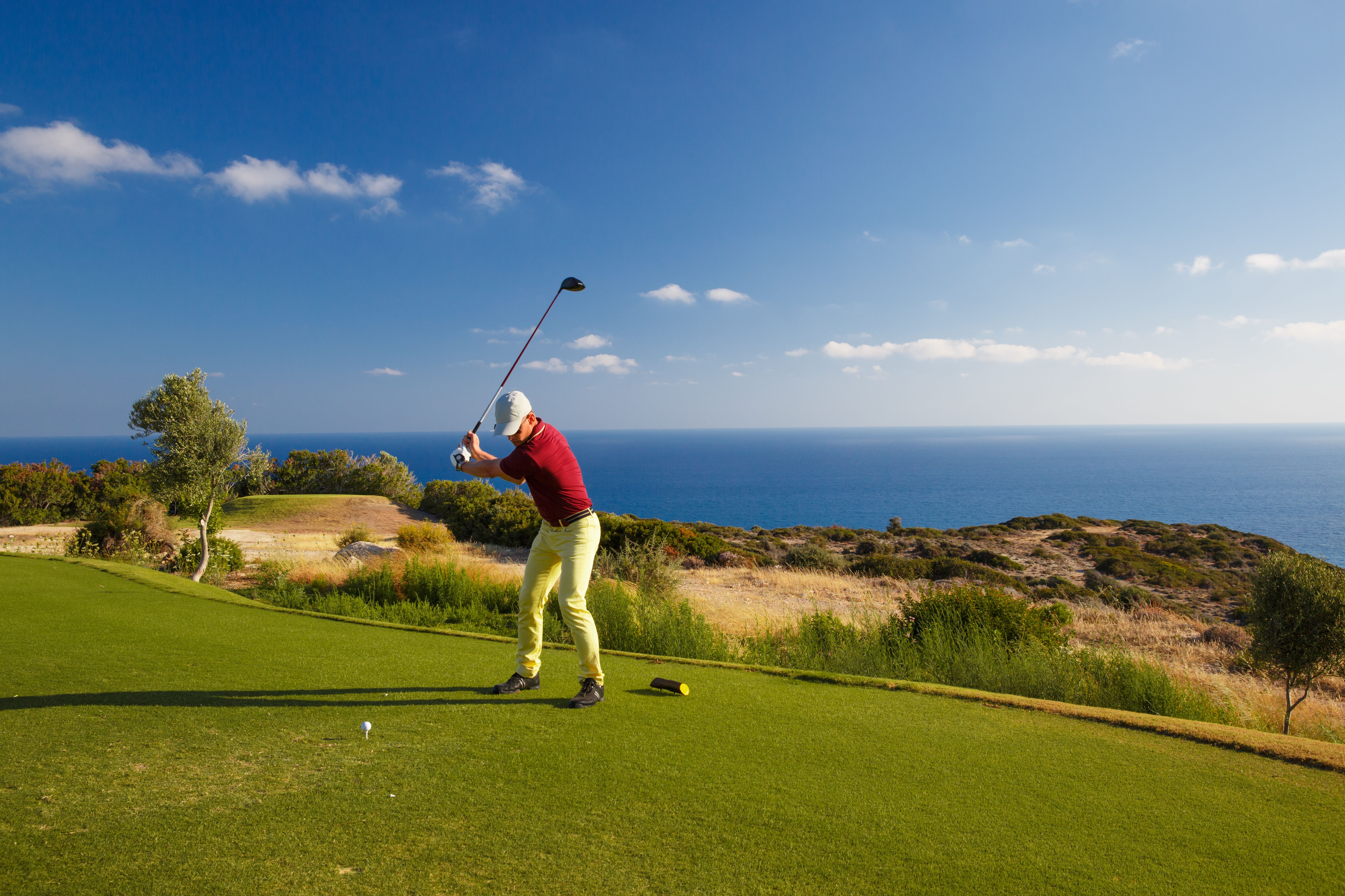A golf player about to hit a tee on a sunny golf course with the sea on the background