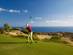 A golf player about to hit a tee on a sunny golf course with the sea on the background