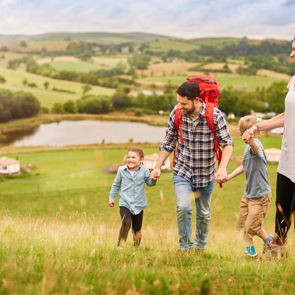 A young family walking up a hill from their campsite with rolling green hills and yurts in the background