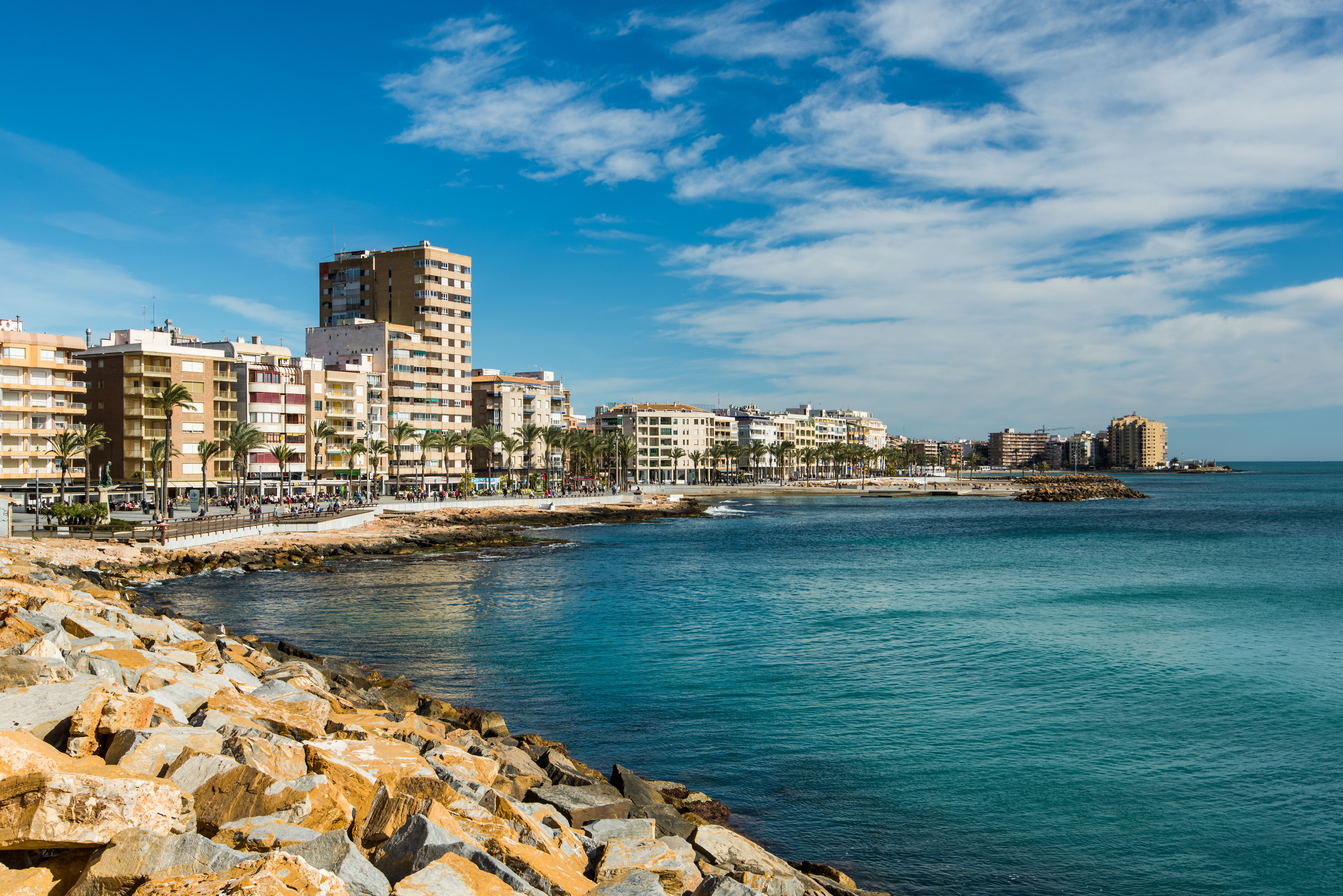 View of a hotel- and apartment-lined beach town in the Costa Blanca on a sunny day.