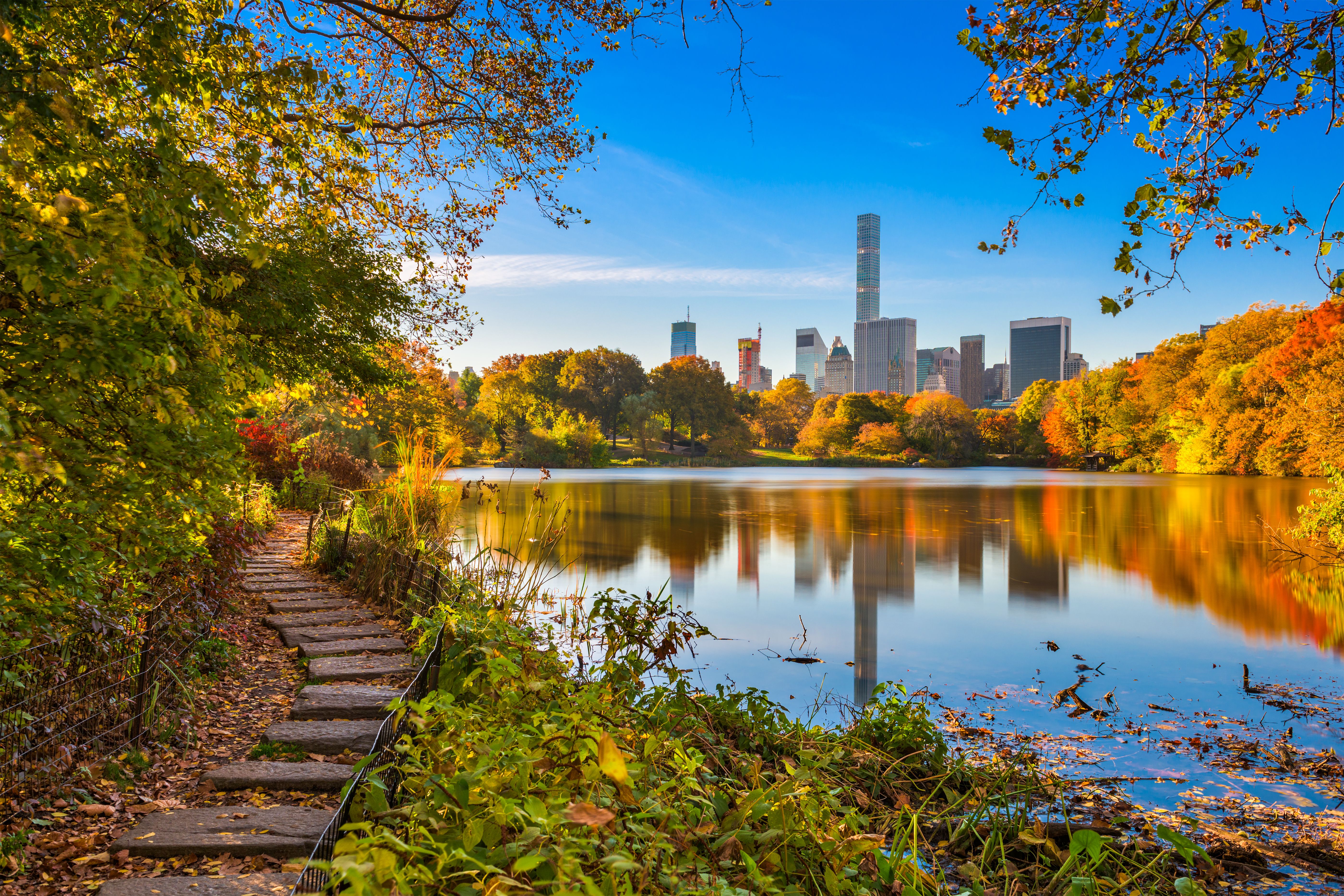 View across a still lake in Central Park with New York's high rises in the background.