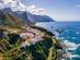 Aerial drone view of a clifftop hamlet surrounded by sharp mountain peaks and the powerful Atlantic Ocean.
