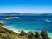 View across a calm bay with yachts bobbing in the distance and a few people on a white-sand beach.