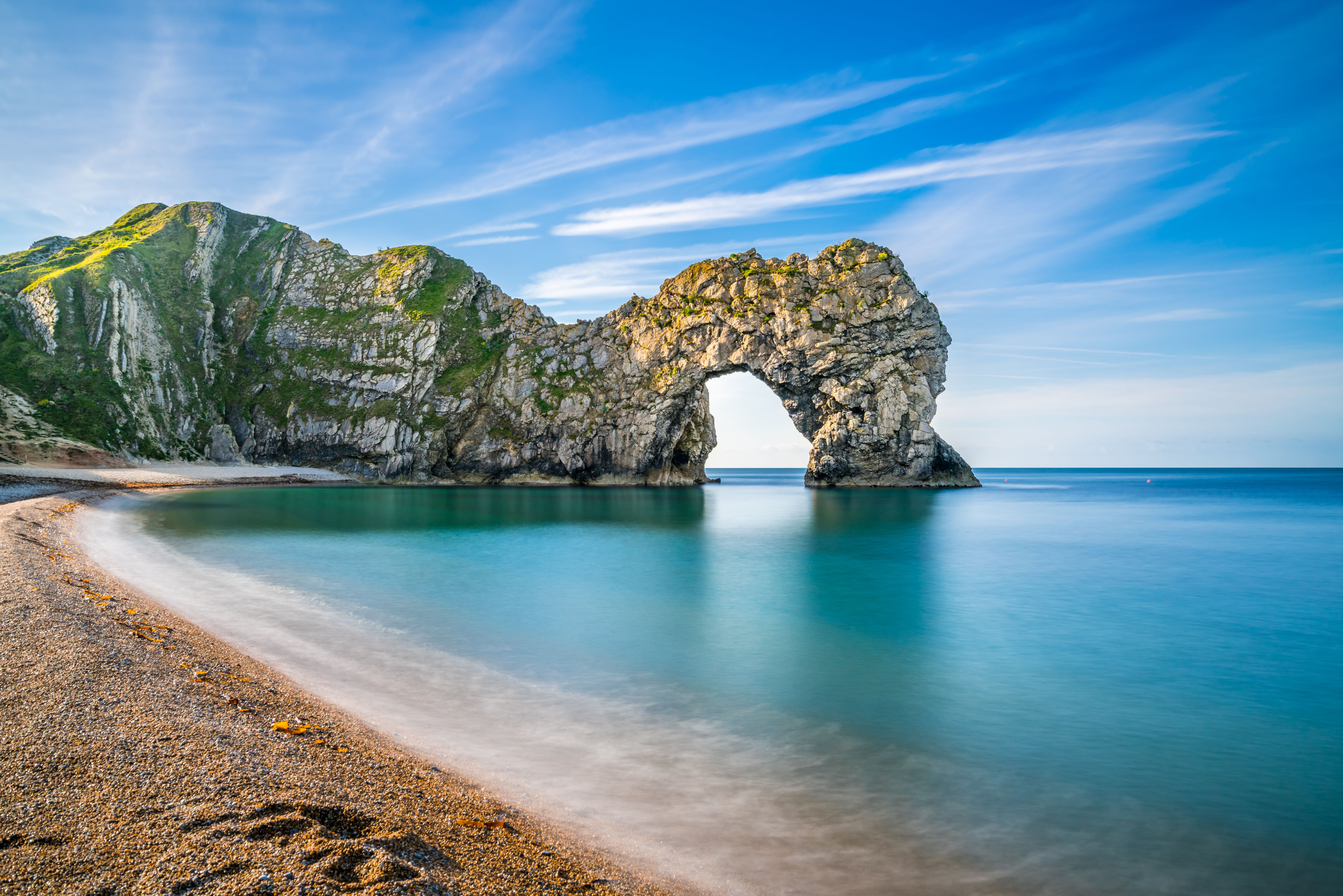 View of calm waters and a natural limestone arch on a pebbly and sandy beach