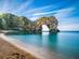 View of calm waters and a natural limestone arch on a pebbly and sandy beach
