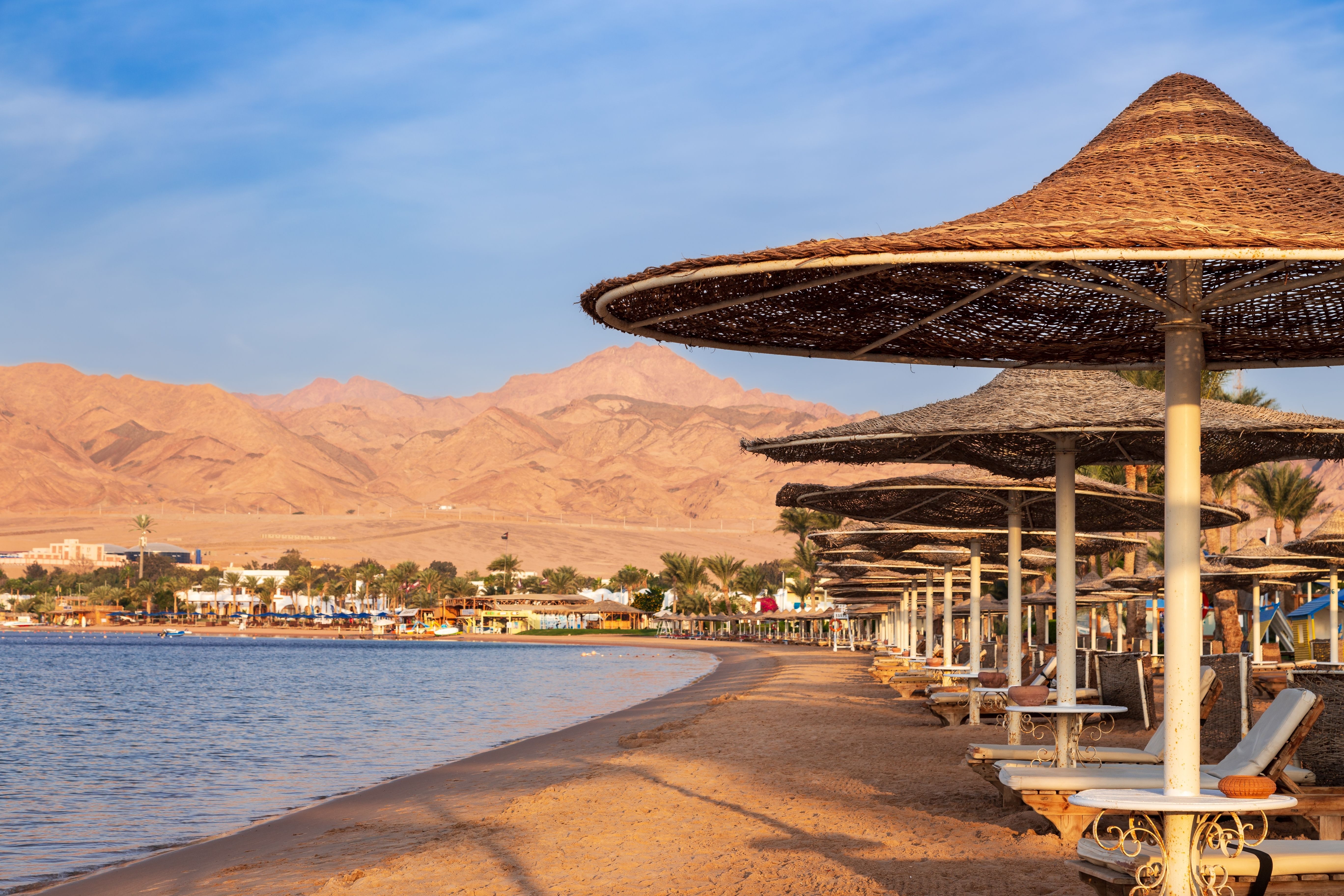 Hotel beach with rows of sun loungers under straw umbrellas against mountains in Dahab, Egypt