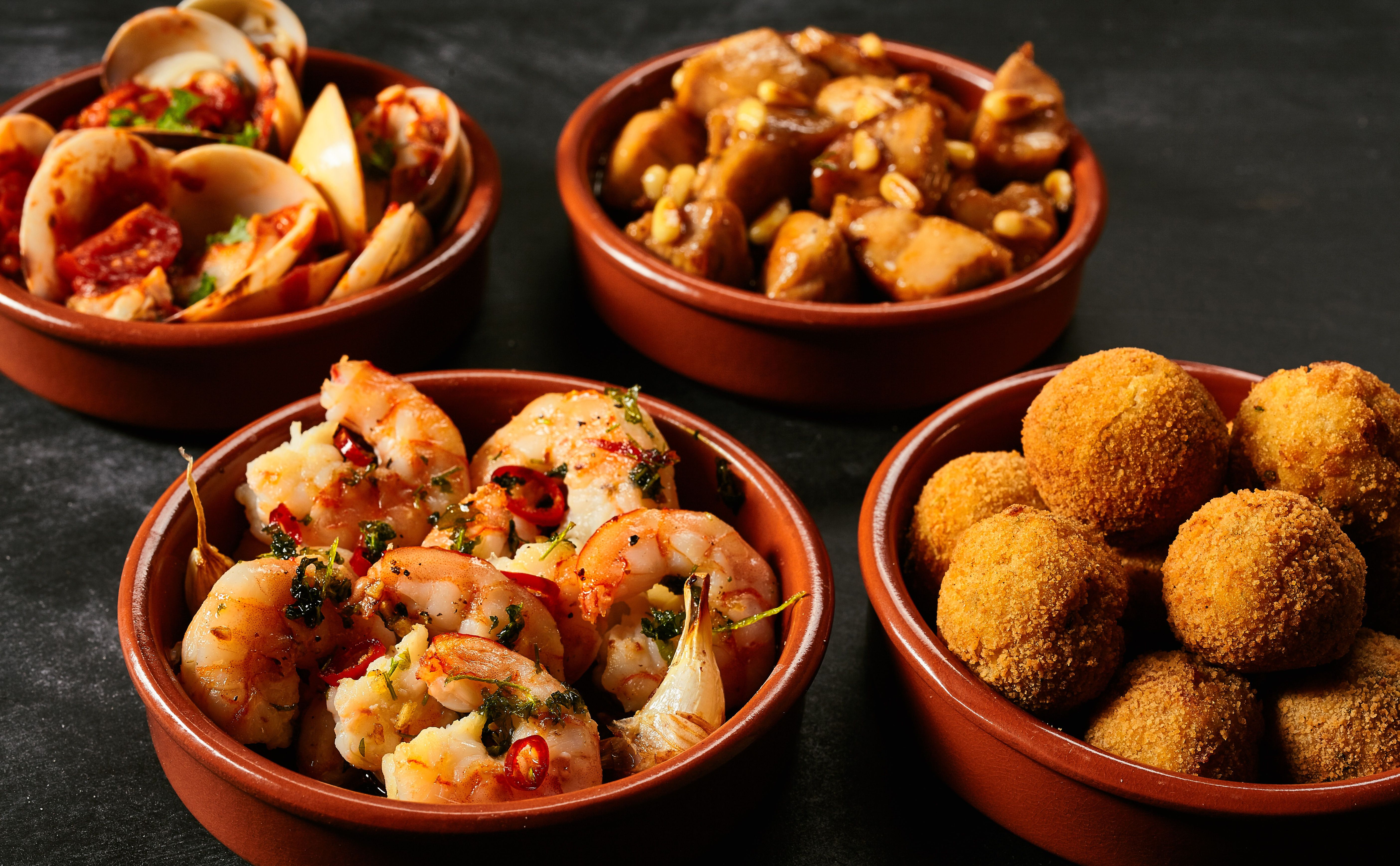 Four terracotta bowls filled with tapas including prawns, clams and croquettes