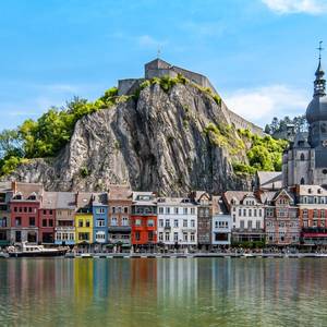 An image of colorful buildings and citadel along the Meuse river in Dinant, Wallonia, Belgium with the reflection of houses in the water on a sunny day