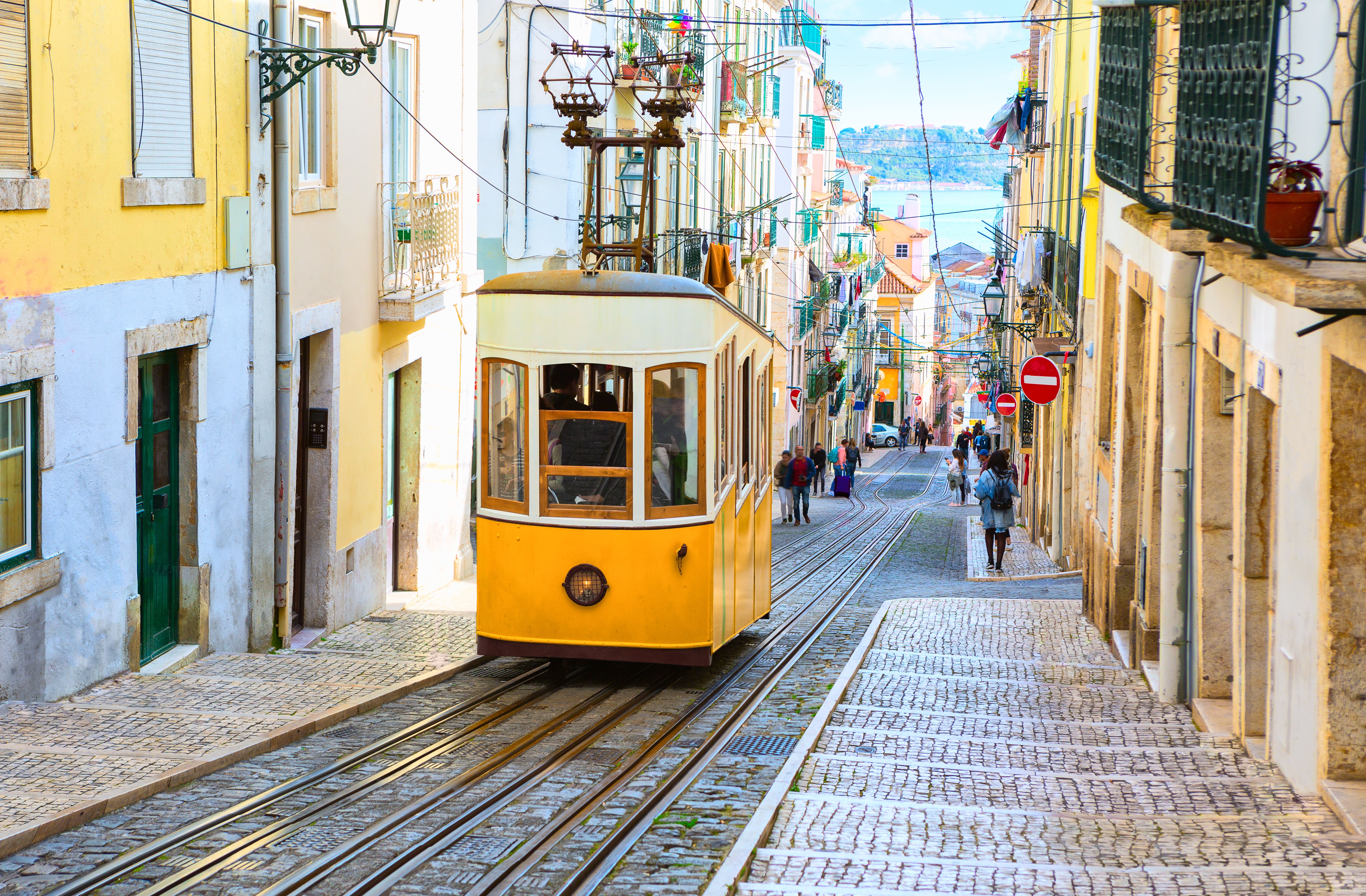 View of a yellow and white tram driving up the steep tracks on a street in Lisbon