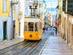 View of a yellow and white tram driving up the steep tracks on a street in Lisbon