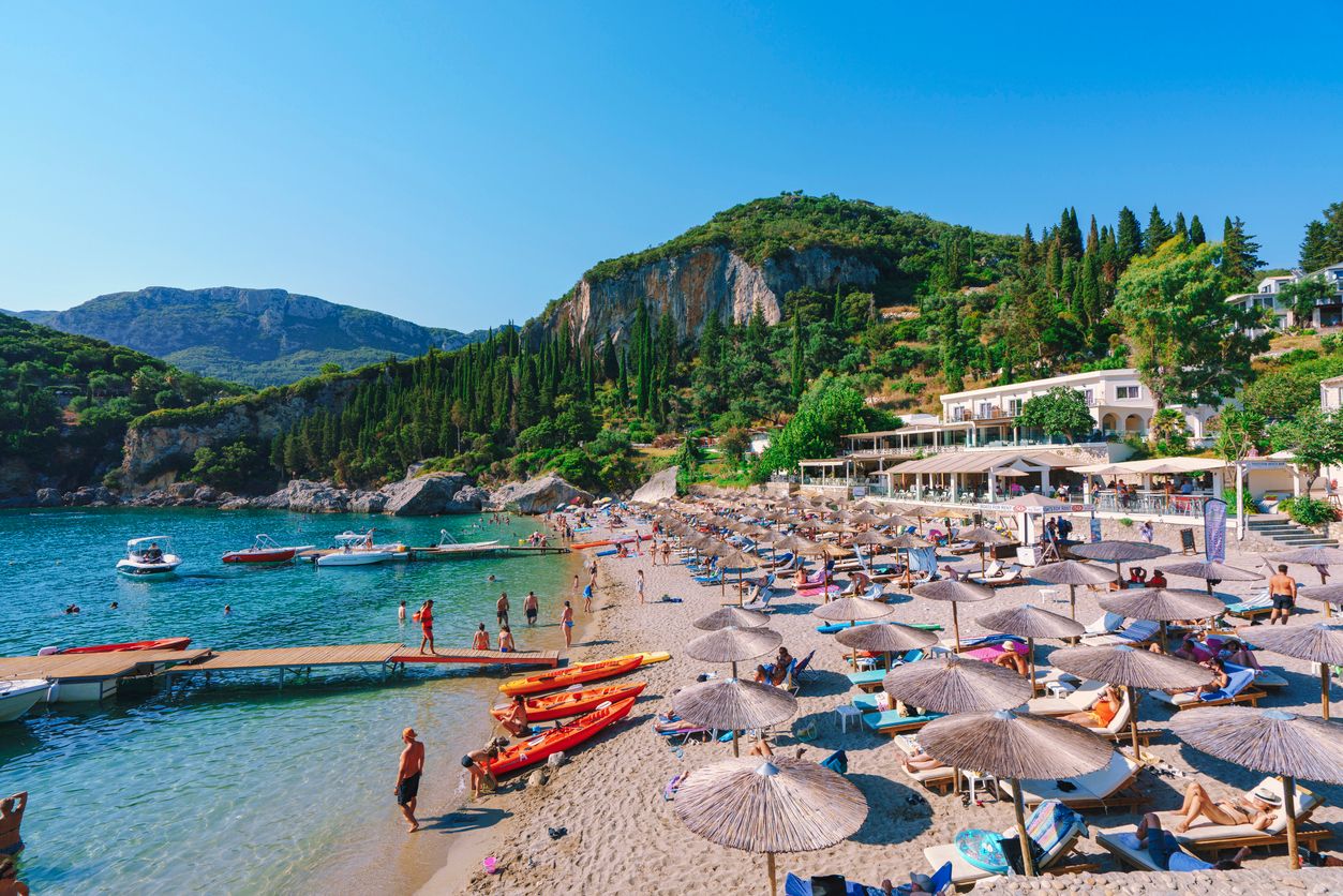 View of sun-loungers and parasols on a sandy Greek beach with kayaks and boats in bobbing in the clear waters