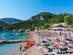 View of sun-loungers and parasols on a sandy Greek beach with kayaks and boats in bobbing in the clear waters