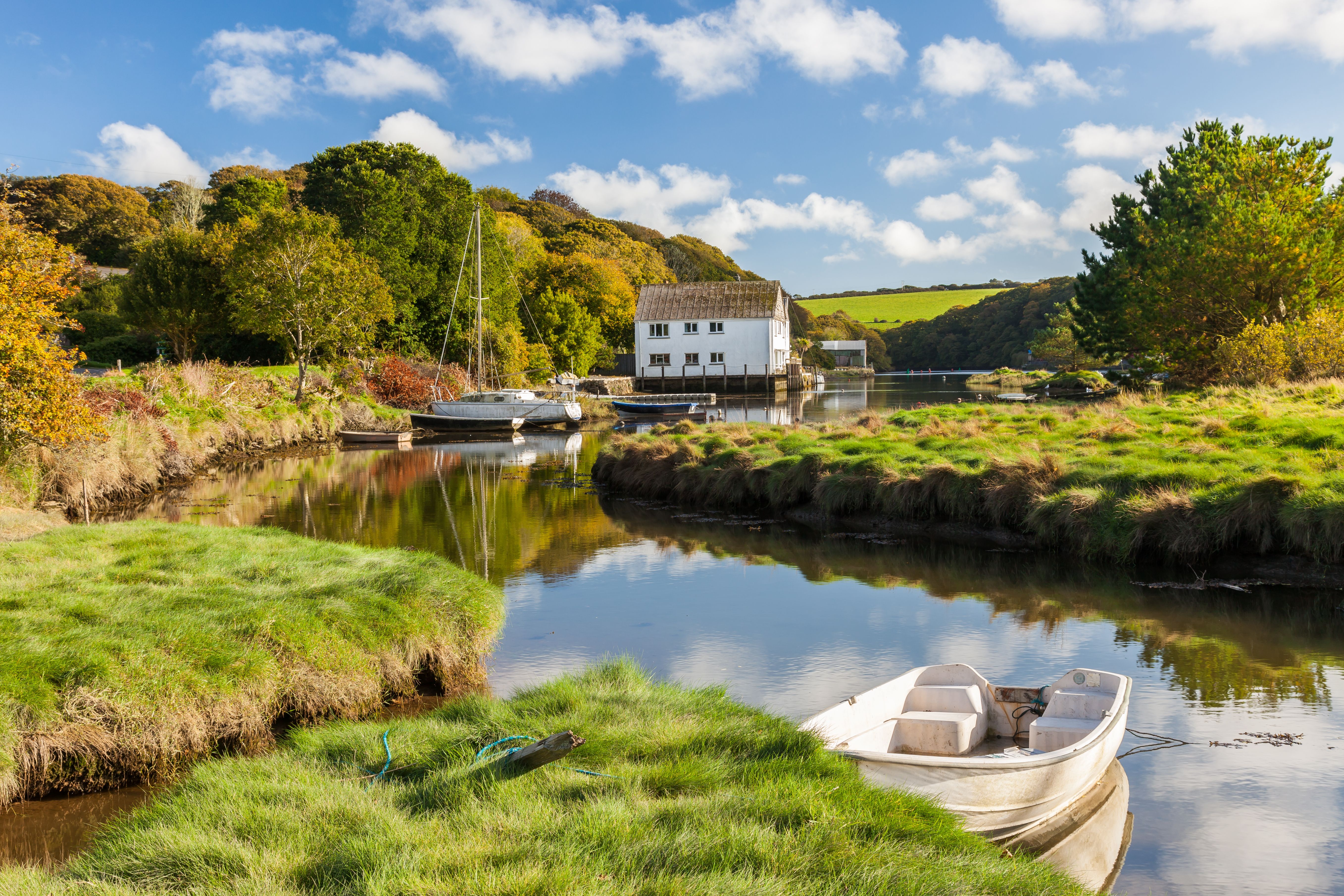 View of a house on the bank of a river that has a small rowboat and is surrounded by lush green countryside.