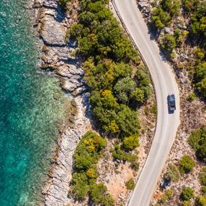 A bird's eye view of a pick-up truck driving along a coastal road in Kefalonia, Greece with calm blue sea