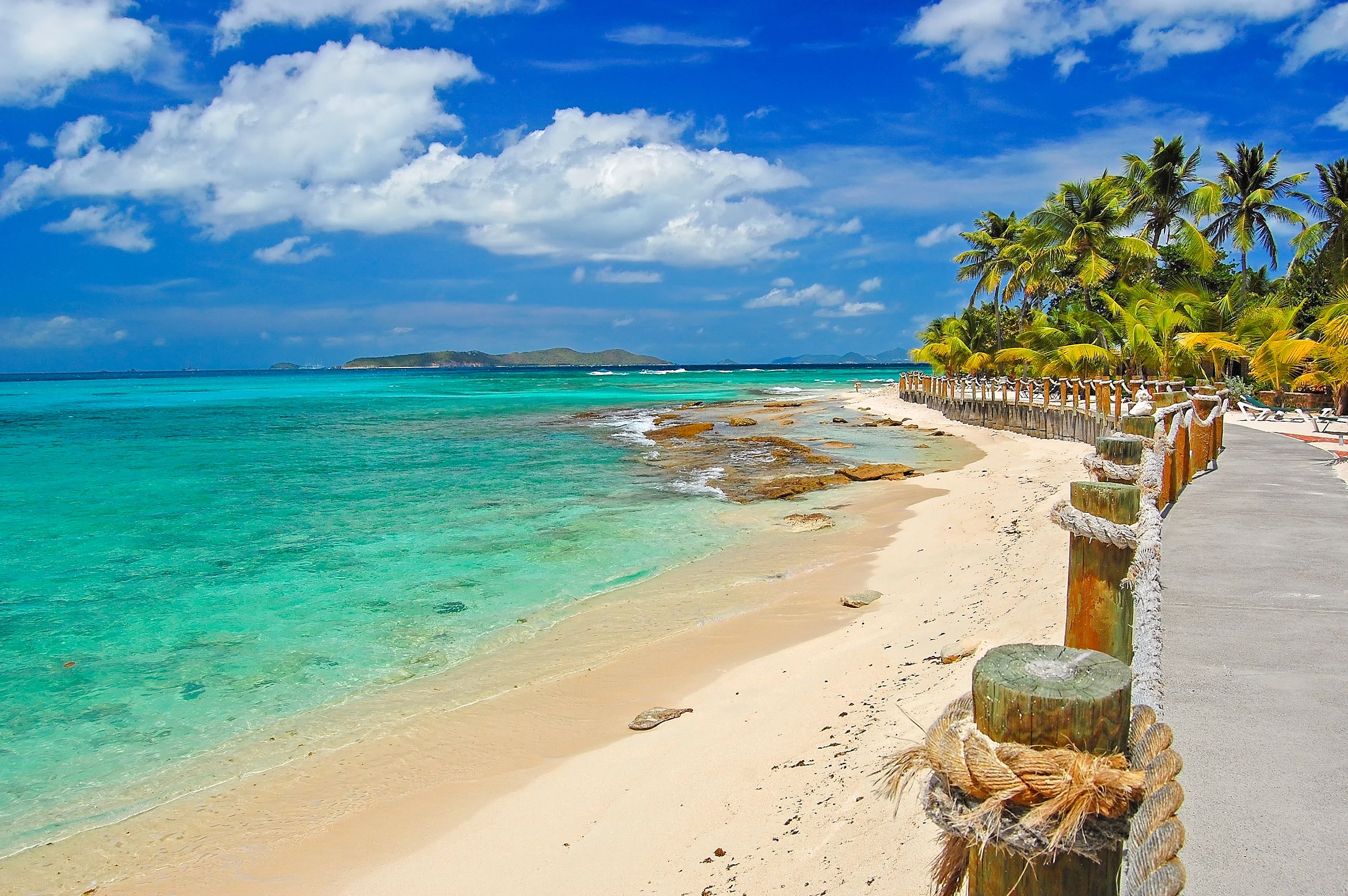 A white-sand beach in St Vincent and the Grenadines in the Caribbean with a wooden walk way and pam trees