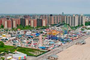 An aerial view of Coney Island amusement park in New York with brightly coloured rides and high-rise buildings in the background