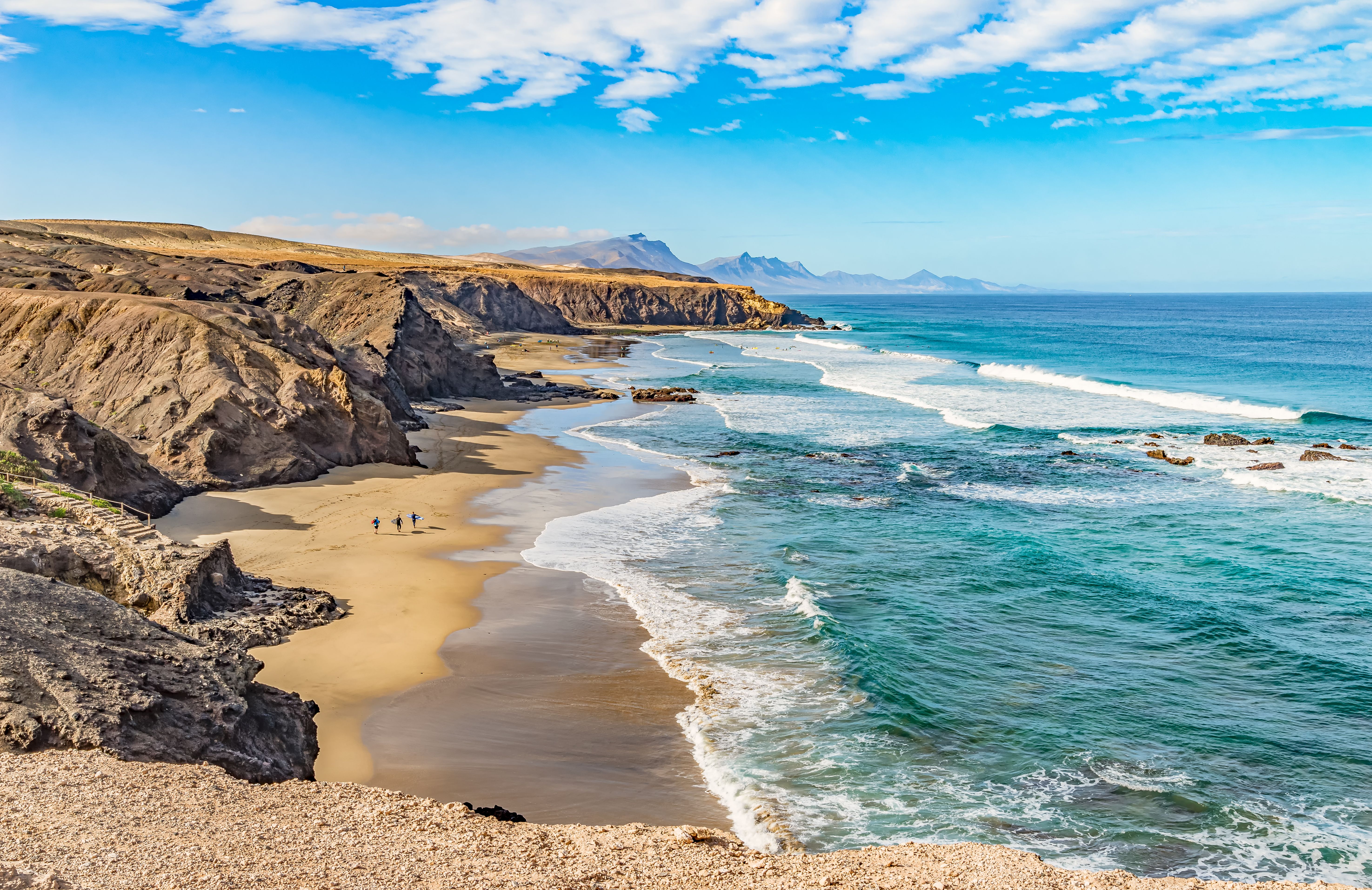 Sweeping view of the wild waves and golden sand of Playa del Viejo Rey beach, which is surrounded by rocky mountains