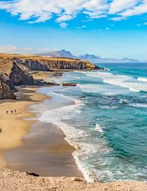 Sweeping view of the wild waves and golden sand of Playa del Viejo Rey beach, which is surrounded by rocky mountains