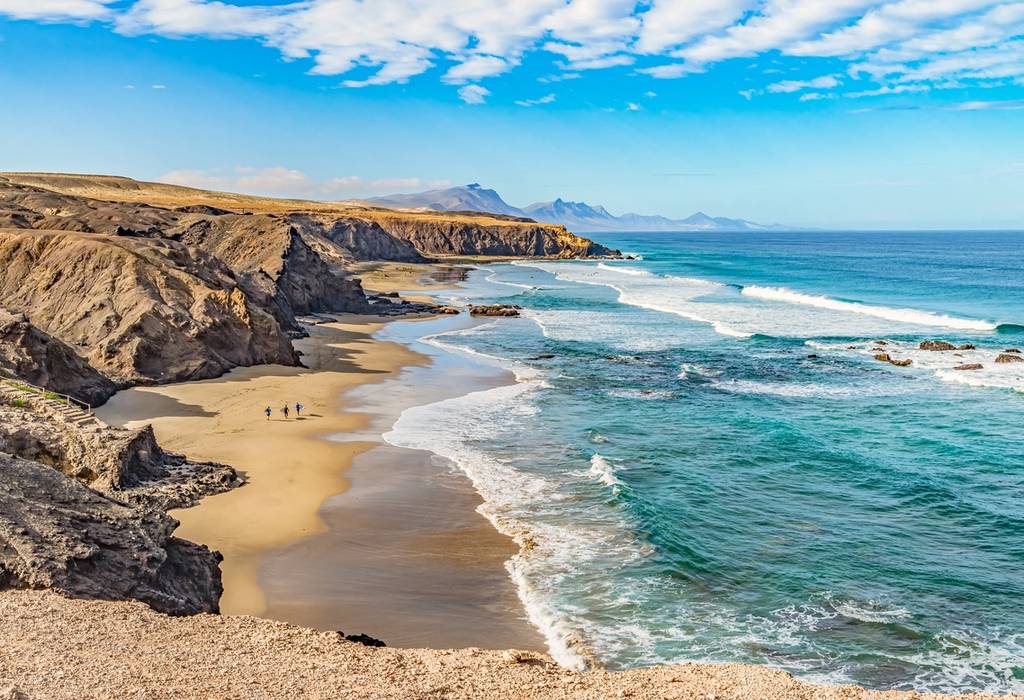 Sweeping view of the wild waves and golden sand of Playa del Viejo Rey beach, which is surrounded by rocky mountains