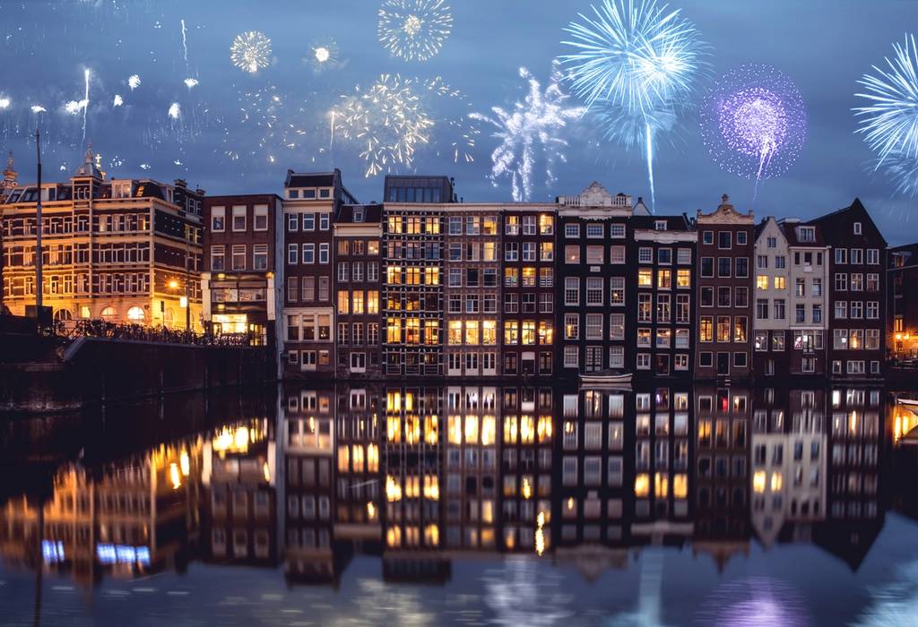 Amsterdam canals and typical houses on a New Year's Eve night celebrations with fireworks in the background and reflection of the houses and fireworks in the canal