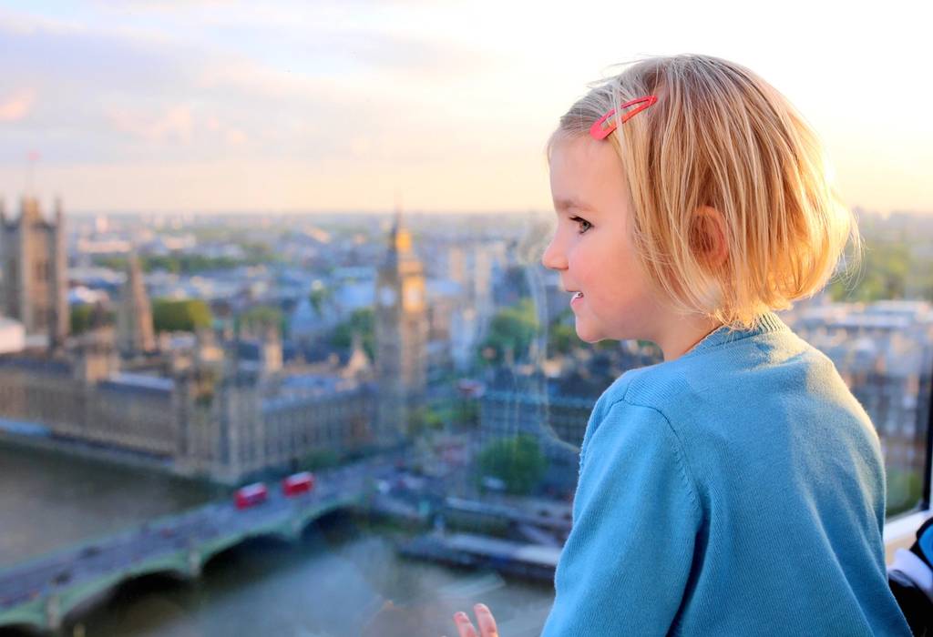 A young girl looks through the window of London Eye wheel out to the Houses of Parliament, Big Ben and the Thames