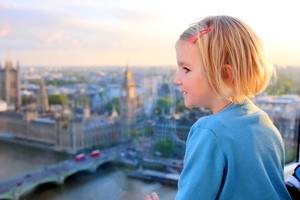 A young girl looks through the window of London Eye wheel out to the Houses of Parliament, Big Ben and the Thames