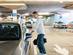 A young man stands in an underground garage with a bag in hand, opening his car door and smiling.