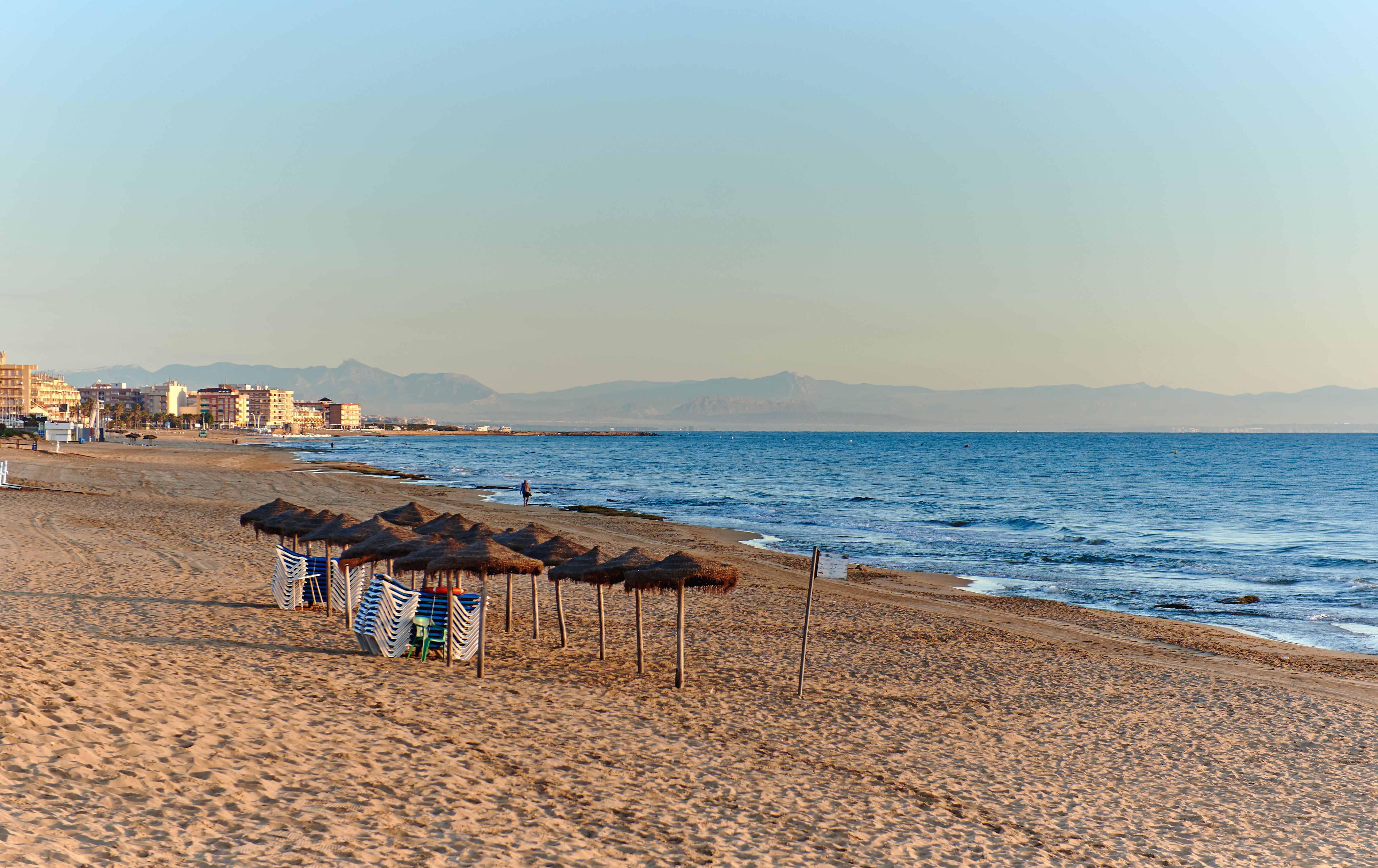 View of a cluster of thatched beach parasols on an empty, sandy beach at sunrise