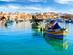 A view looking across the water of Marsaxlokk Fishing Village in Malta with colourful traditional fishing boats moored in the harbour